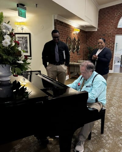 Resident playing piano with staff and more residents nearby