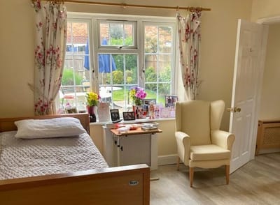 A cozy resident room with a bed and chair by the window