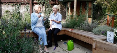 Resident enjoying tea with a caregiver in a garden