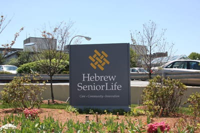 Hebrew SeniorLife, Nursing Home in Boston, MA — Facility logo on a sign with landscaping