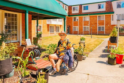 Resident in a wheelchair outside the facility with planters