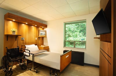 A well-furnished resident room with a wheelchair and window view