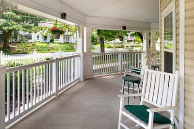 Covered porch area with rocking chairs and view of landscaping