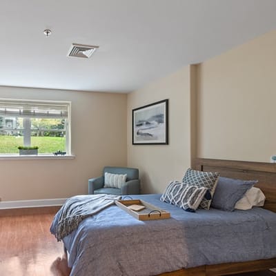 Bright interior of a private resident room with bed and chair