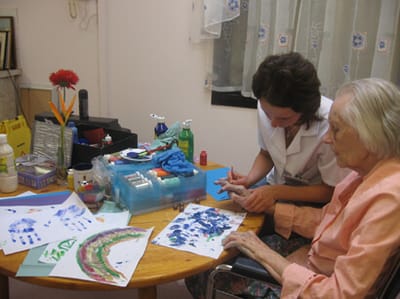 An elderly woman participating in an art activity with a staff member