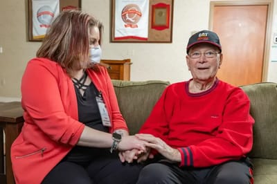 Caregiver and elderly resident sitting together and holding hands in a cozy setting
