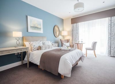 A well-decorated private resident room with a bed and seating area