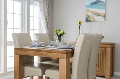 A modern dining room with a wooden table and cream chairs, decorated with flowers and tableware.