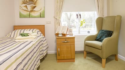 A cozy resident room with a bed and armchair