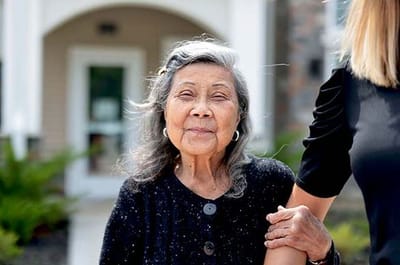Senior resident smiling in front of the facility entrance