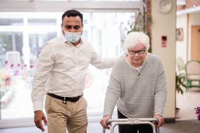A staff member assisting a resident with a walker in a common area