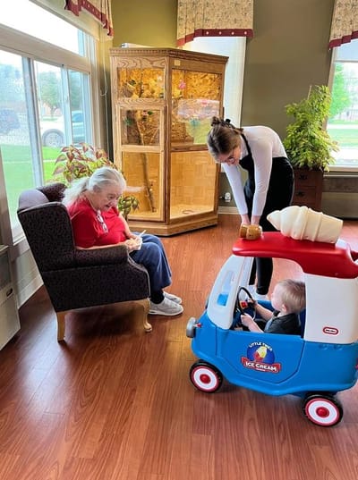 Senior resident enjoying a visit from a child in a toy car