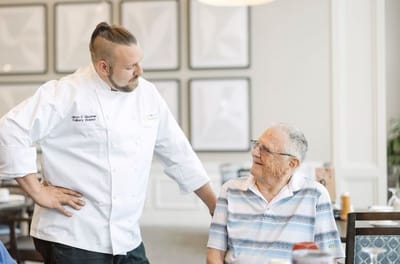 Chef interacting with a senior resident in a dining area