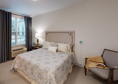 A cozy private resident room with a bed and chair
