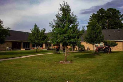 Exterior view of a senior living facility with green lawn and trees