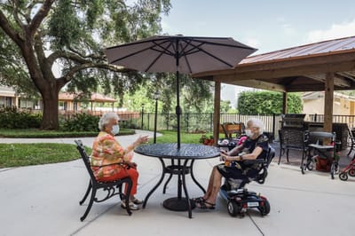 Two residents chatting under an outdoor umbrella