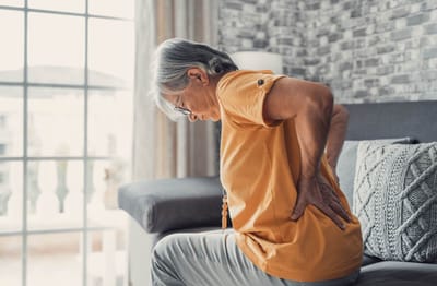 Elderly woman sitting with a pained expression on a couch