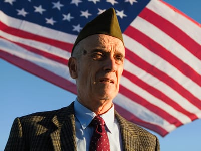 Elderly man in military attire with American flag backdrop