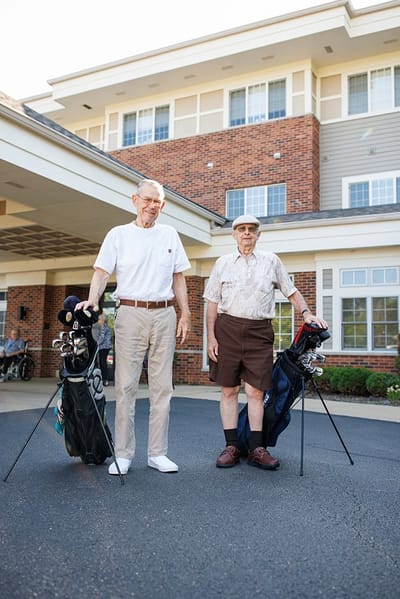 Two seniors with golf clubs in front of the building