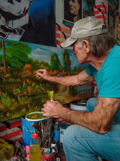 An elderly man painting outdoors in a colorful garden