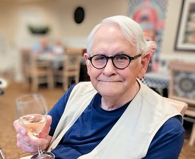 A smiling resident holding a glass of wine in a social area