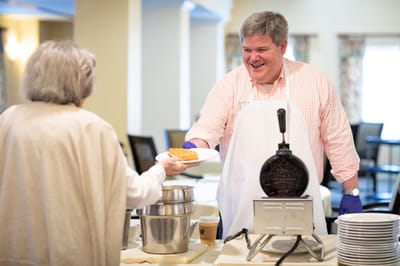 Staff serving food to a resident in a bright dining area