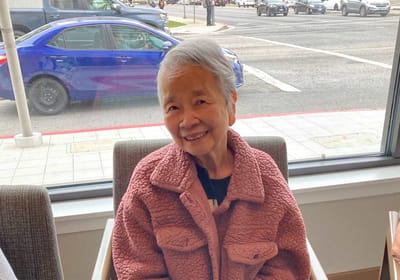 Smiling elderly woman sitting indoors by a window