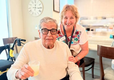 An elderly man smiles with a staff member in a common area
