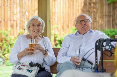 Two seniors enjoying drinks under a shaded area
