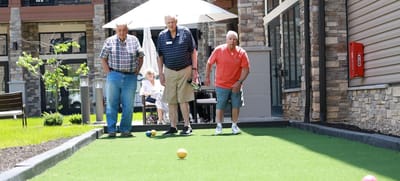 Three residents playing outdoor bocce ball in a facility garden