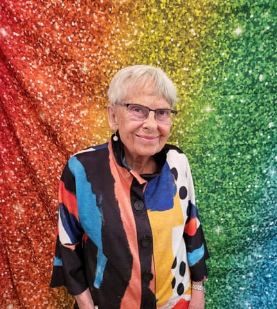 An elderly woman smiling in front of a colorful background
