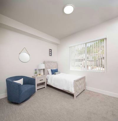 Brightly lit private resident room with a bed and armchair