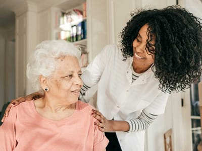 Caregiver smiling while assisting an elderly woman