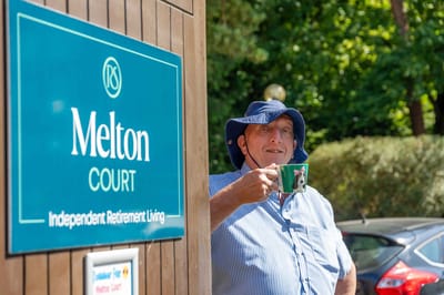 Resident enjoying a drink by the facility sign outdoors
