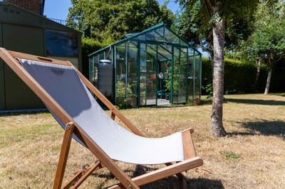 A deck chair in a sunny garden with a greenhouse in the background