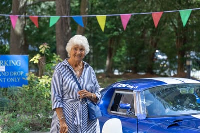 A resident smiling near a blue sports car in an outdoor area