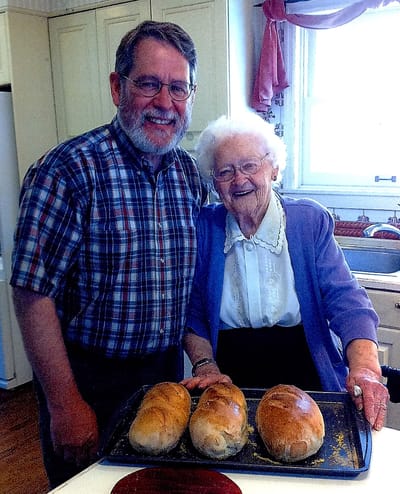 A woman and man smiling with fresh-baked loaves of bread