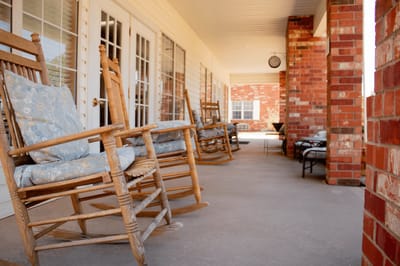 Rocking chairs on a porch outside a building.