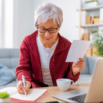 Senior woman writing notes in a cozy setting.