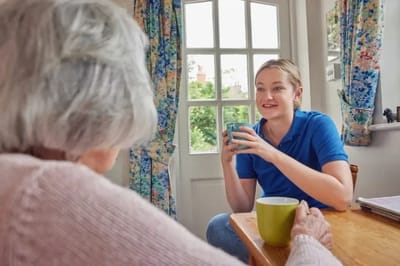 Caregiver chatting with elderly resident over tea.