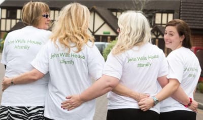Four women wearing matching shirts, smiling outdoors.