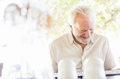 Senior man laughing outdoors in a casual setting.