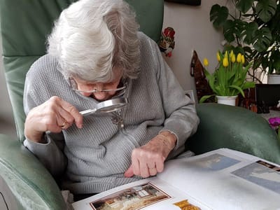 Elderly woman examining a photo album with a magnifying glass.