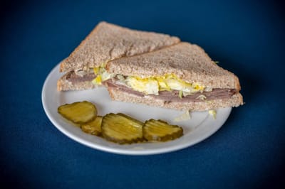 Plate of sandwich and pickles on a blue tablecloth.