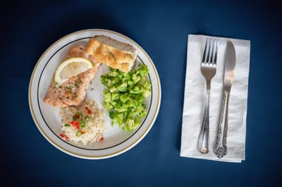 A plate of salmon, rice, and salad with utensils.