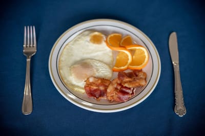 A plate of breakfast with eggs, bacon, and oranges.