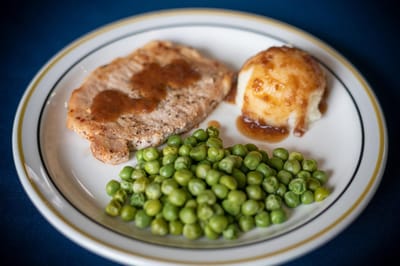 Plate of food with pork, mashed potatoes, and peas.