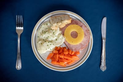 A plated meal with ham, mashed potatoes, carrots, and bread.