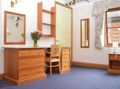 A neatly arranged resident room with a desk and flowers.