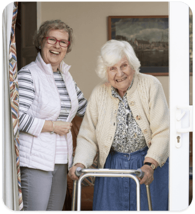 Caregiver smiling with an elderly resident at the door.